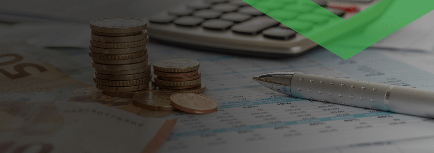 Gestapelte Euromünzen, ein Kugelschreiber und ein Taschenrechner liegen auf einem Finanzdokument mit Tabellen. Die Szene symbolisiert eine Sondertilgung – also eine außerplanmäßige Rückzahlung eines Teils eines Kredits.