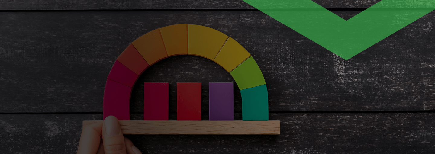 Eine Hand hält ein buntes Halbkreis-Diagramm aus Holz, das von Rot über Gelb zu Grün verläuft. In der Mitte stehen vier unterschiedlich hohe Balken. Die Szene symbolisiert die Überprüfung der Bonität, also der Kreditwürdigkeit einer Person oder eines Unternehmens.
