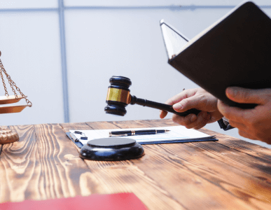 Ein Richter oder Beamter hält einen Holzhammer und ein Notizbuch über einem Schreibtisch mit Waage, Klemmbrett und Schreibutensilien. Die Szene symbolisiert eine Zwangsvollstreckung – also die gerichtliche Durchsetzung von Forderungen gegenüber Schuldnern.