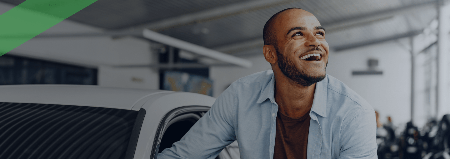 Ein junger Mann steht lächelnd neben einem weißen Auto und hält die Fahrertür offen. Die Szene symbolisiert die Übergabe oder Nutzung eines Fahrzeugs, etwa im Zusammenhang mit einem Eigentumsvorbehalt, bei dem das Auto erst mit vollständiger Zahlung in das Eigentum des Käufers übergeht.