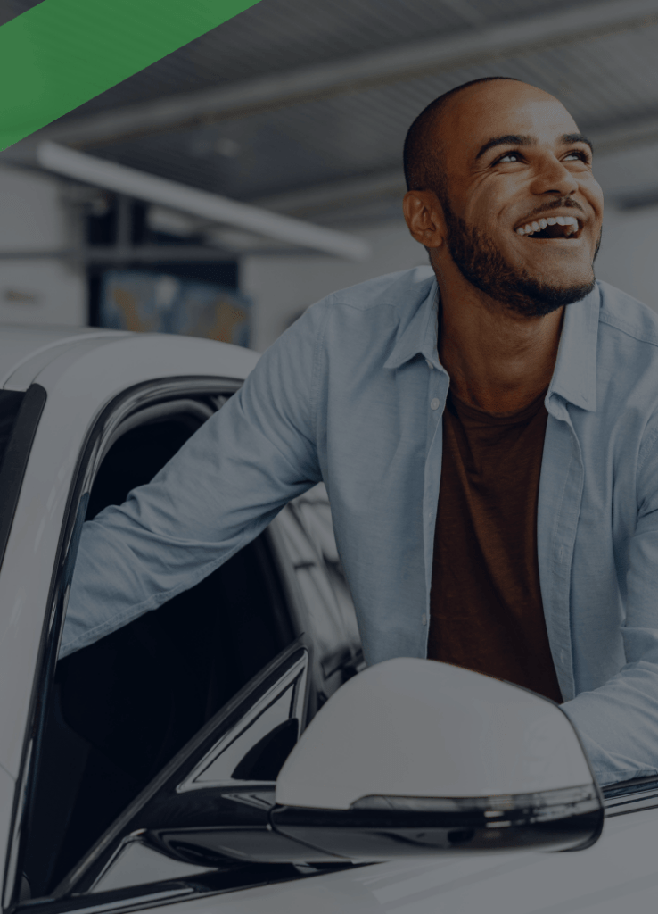 Ein junger Mann steht lächelnd neben einem weißen Auto und hält die Fahrertür offen. Die Szene symbolisiert die Übergabe oder Nutzung eines Fahrzeugs, etwa im Zusammenhang mit einem Eigentumsvorbehalt, bei dem das Auto erst mit vollständiger Zahlung in das Eigentum des Käufers übergeht.