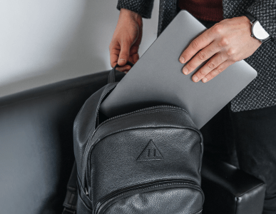 Eine Person steckt ein silbernes Laptop in einen schwarzen Rucksack. Die Szene symbolisiert einen kürzlich erfolgten Kauf, möglicherweise über einen Finanzkauf oder Ratenkredit finanziert.