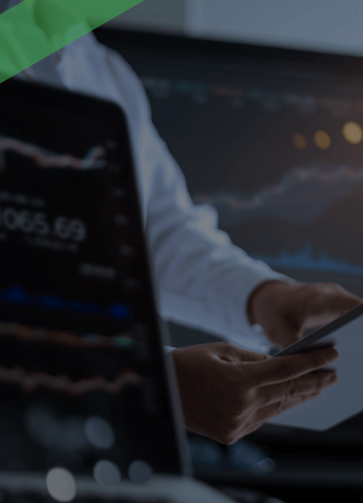 Eine Person hält ein Tablet in der Hand und beobachtet Finanz- oder Börsendaten auf einem großen Bildschirm im Hintergrund. Im Vordergrund ist ein Laptop mit ähnlichen Kursgrafiken zu sehen. Die Szene symbolisiert Aktivitäten auf dem Kreditmarkt oder die Analyse von Finanz- und Kapitalmarktdaten.