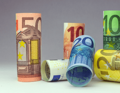 Verschiedenfarbige Euro-Geldscheine sind zu Rollen geformt und stehen oder liegen aufrecht nebeneinander. Die Szene symbolisiert den Roll-over-Kredit, bei dem ein Kreditbetrag regelmäßig verlängert und zu variablen Konditionen neu verzinst wird.