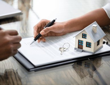 Eine Person unterschreibt einen Vertrag auf einem Klemmbrett, daneben liegen ein Schlüsselbund und ein kleines Modellhaus. Die Szene symbolisiert eine Immobilien- oder Kreditrefinanzierung, bei der bestehende Kreditkonditionen durch neue ersetzt werden.