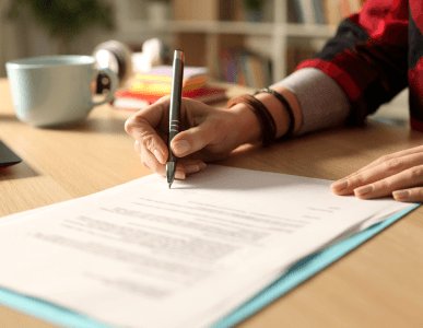 Eine Person unterschreibt ein offizielles Dokument auf einem Schreibtisch, daneben liegen eine Tasse und Schreibutensilien. Die Szene symbolisiert die Unterzeichnung einer Bürgschaft, bei der jemand für die Verpflichtungen einer dritten Person haftet.