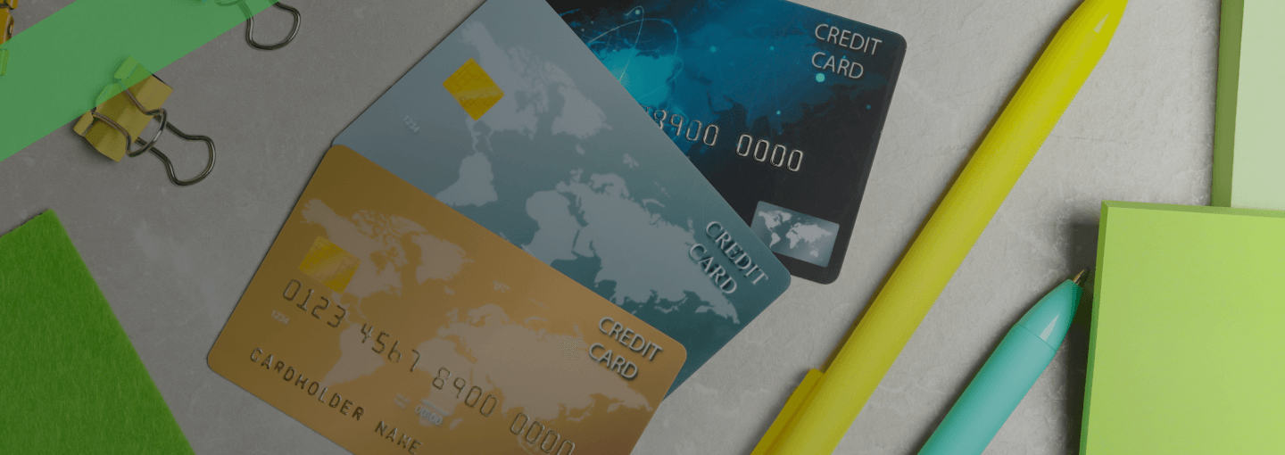 Drei Kreditkarten liegen auf einem Schreibtisch zwischen Büroartikeln wie Stiften, Papierklammern und Haftnotizen. Die Szene symbolisiert die Konsolidierung mehrerer Kreditverpflichtungen, etwa durch Umschuldung oder Zusammenfassung von Kreditkartenschulden.