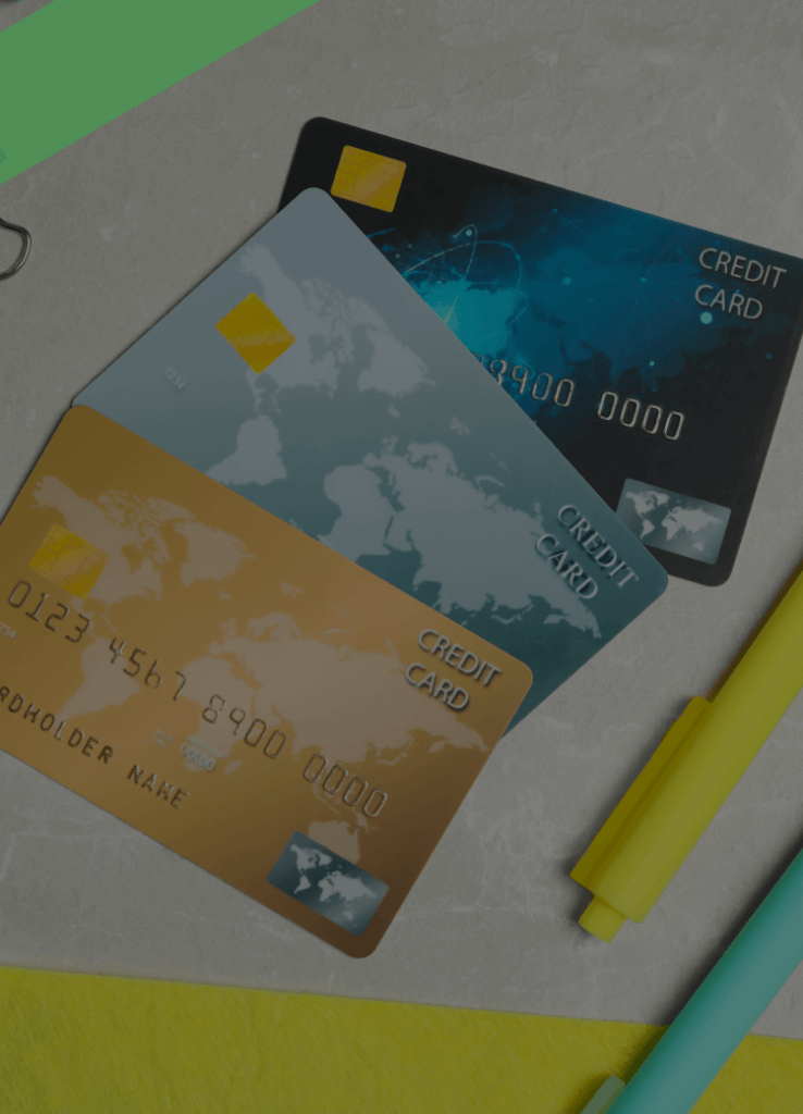 Drei Kreditkarten liegen auf einem Schreibtisch zwischen Büroartikeln wie Stiften, Papierklammern und Haftnotizen. Die Szene symbolisiert die Konsolidierung mehrerer Kreditverpflichtungen, etwa durch Umschuldung oder Zusammenfassung von Kreditkartenschulden.