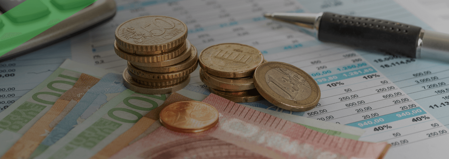 Auf einem Schreibtisch liegen gestapelte Euromünzen und -scheine, daneben ein Kugelschreiber, ein Taschenrechner und ein Formular mit Zahlen. Die Szene symbolisiert die finanzielle Abtretung von Gehalt oder Lohn, wie sie bei einer Lohnabtretung im Kreditkontext üblich ist.