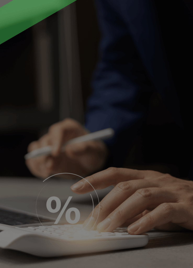 Eine Person tippt auf einem weißen Taschenrechner mit eingeblendetem Prozentzeichen, während sie mit der anderen Hand Notizen am Laptop macht. Die Szene symbolisiert die Berechnung des Nominalzinses, also des reinen Zinssatzes ohne Berücksichtigung weiterer Kosten.