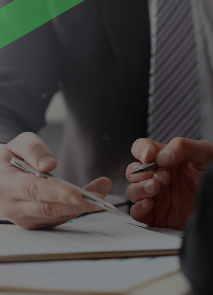 Zwei Personen im Anzug besprechen gemeinsam ein Dokument am Schreibtisch. Eine Person hält einen Stift und deutet auf das Papier, während die andere aufmerksam zuhört. Die Szene symbolisiert ein Beratungsgespräch zu einem speziellen Kredit, etwa einem Organkredit im Unternehmenskontext.