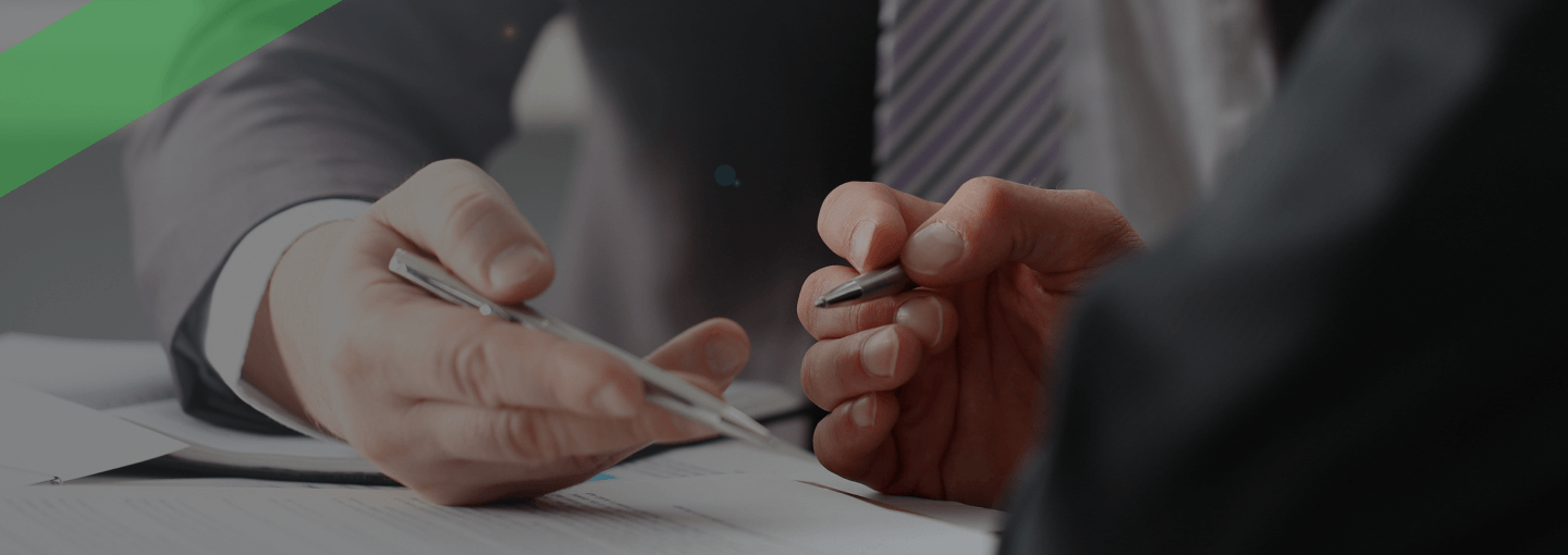 Zwei Personen im Anzug besprechen gemeinsam ein Dokument am Schreibtisch. Eine Person hält einen Stift und deutet auf das Papier, während die andere aufmerksam zuhört. Die Szene symbolisiert ein Beratungsgespräch zu einem speziellen Kredit, etwa einem Organkredit im Unternehmenskontext.