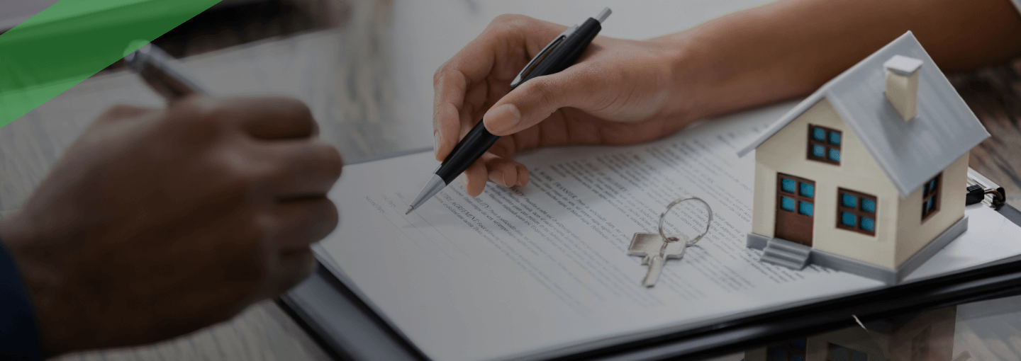 Eine Person unterschreibt einen Vertrag auf einem Klemmbrett, daneben liegen ein Schlüsselbund und ein kleines Modellhaus. Die Szene symbolisiert eine Immobilien- oder Kreditrefinanzierung, bei der bestehende Kreditkonditionen durch neue ersetzt werden.