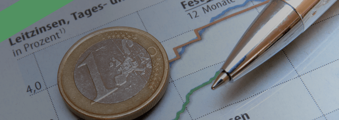 Ein 1-Euro-Stück und ein Kugelschreiber liegen auf einem Diagramm, das die Entwicklung von Leitzinsen, Tagesgeld- und Festgeldzinsen zeigt. Die Szene symbolisiert die Bedeutung des Sollzinses als Bestandteil der Kreditkosten.