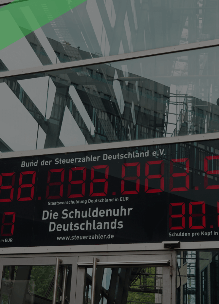 Die Schuldenuhr des Bundes der Steuerzahler Deutschlands ist an der Glasfassade eines Gebäudes angebracht und zeigt in roten Ziffern die aktuelle Staatsverschuldung sowie die Schulden pro Kopf an. Die Szene symbolisiert das Ausmaß der öffentlichen Verschuldung in Deutschland.