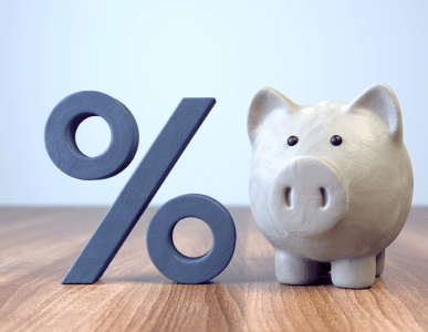 Ein weißes Sparschwein steht auf einem Holztisch neben einem großen Prozentzeichen. Die Szene symbolisiert ein variables Darlehen, bei dem sich die Zinshöhe während der Laufzeit ändern kann.