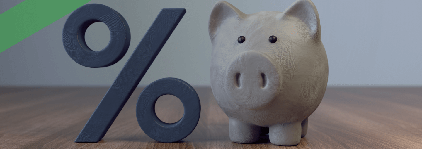 Ein weißes Sparschwein steht auf einem Holztisch neben einem großen Prozentzeichen. Die Szene symbolisiert ein variables Darlehen, bei dem sich die Zinshöhe während der Laufzeit ändern kann.