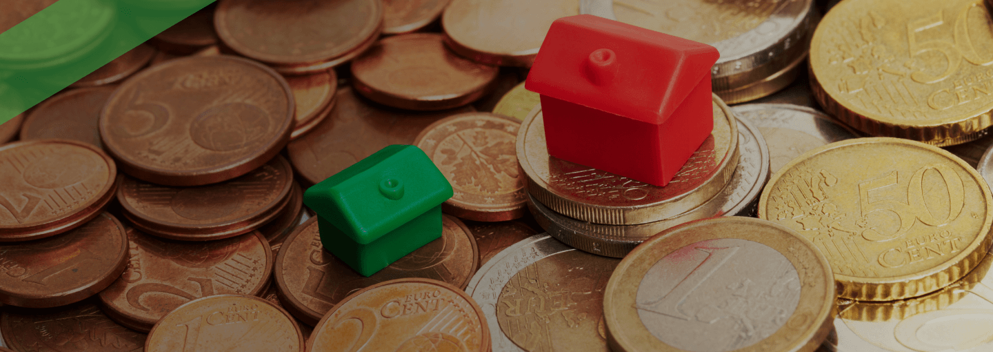 Zwei unterschiedlich große Spielzeughäuser stehen auf einem Haufen Euro-Münzen. Die Szene symbolisiert die Zinsspanne, also die Differenz zwischen Soll- und Habenzinsen bei der Kreditvergabe durch Banken.