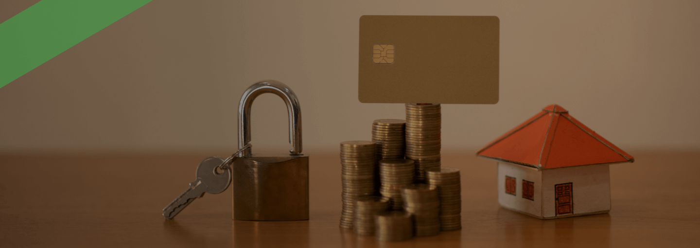 Symbolische Darstellung finanzieller Themen: Ein Stapel Euro-Münzen mit einer Kreditkarte darauf steht neben einem Vorhängeschloss mit Schlüssel sowie einem kleinen Modellhaus mit rotem Dach. Die Bildkomposition verweist auf Themen wie Kreditsicherheit, Immobilienfinanzierung oder Ablösebescheinigung bei Krediten.