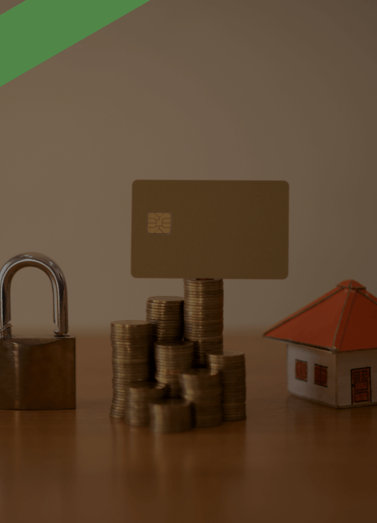 Symbolische Darstellung finanzieller Themen: Ein Stapel Euro-Münzen mit einer Kreditkarte darauf steht neben einem Vorhängeschloss mit Schlüssel sowie einem kleinen Modellhaus mit rotem Dach. Die Bildkomposition verweist auf Themen wie Kreditsicherheit, Immobilienfinanzierung oder Ablösebescheinigung bei Krediten.