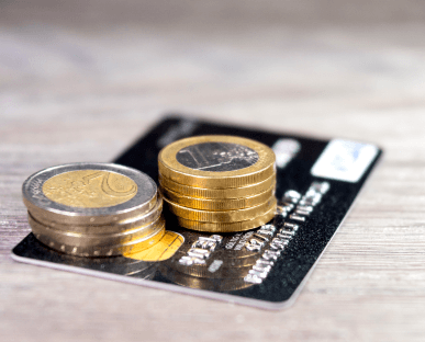 Gestapelte Euro-Münzen liegen auf einer Kreditkarte, die auf einem Holztisch platziert ist. Die Szene symbolisiert finanzielle Transaktionen, Kreditverfügbarkeit oder flexible Zahlungsmöglichkeiten wie bei einem Abruf- oder Rahmenkredit.