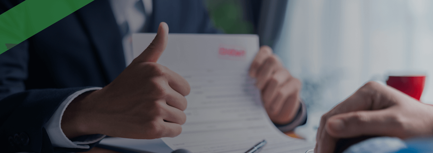 Ein Berater in Anzug hält ein Vertragsdokument und zeigt mit dem Daumen nach oben. Auf dem Tisch liegen Unterlagen, ein Stempel, ein Taschenrechner und ein Klemmbrett. Die Szene symbolisiert die Genehmigung oder den Abschluss eines Investitionskredits zur Finanzierung geschäftlicher Vorhaben.