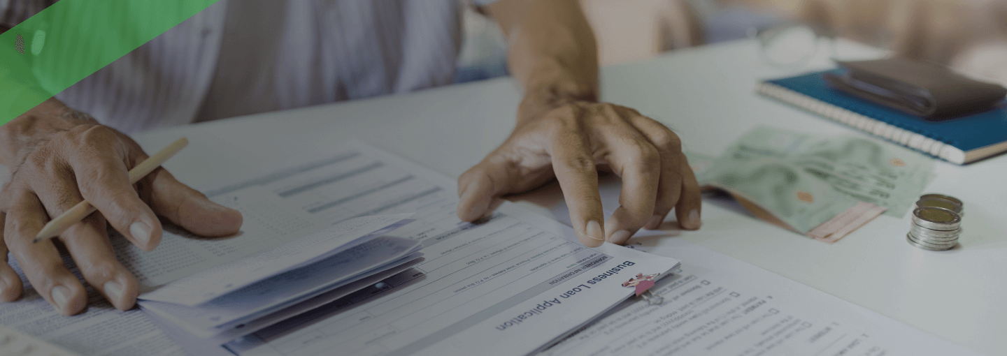 Eine Person überprüft verschiedene Dokumente und Formulare auf einem Tisch, während sie mit einem Stift Notizen macht. Im Vordergrund liegt ein Umschlag mit der Aufschrift „Ihre Kreditentscheidung“. Die Szene symbolisiert die Prüfung und Entscheidungsfindung im Rahmen eines Kreditantrags.