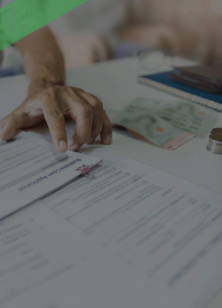Eine Person überprüft verschiedene Dokumente und Formulare auf einem Tisch, während sie mit einem Stift Notizen macht. Im Vordergrund liegt ein Umschlag mit der Aufschrift „Ihre Kreditentscheidung“. Die Szene symbolisiert die Prüfung und Entscheidungsfindung im Rahmen eines Kreditantrags.
