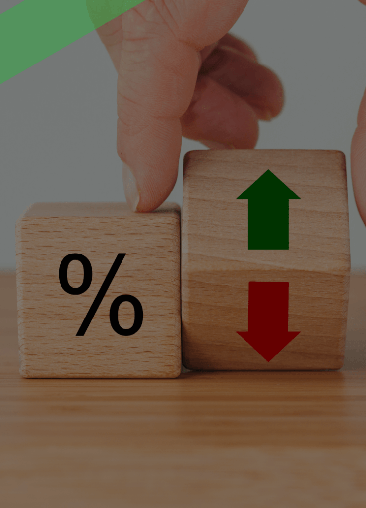 Zwei Holzklötze stehen auf einem Tisch: Einer zeigt ein Prozentzeichen, der andere grüne und rote Pfeile für Steigen und Sinken. Eine Hand bewegt einen der Klötze. Die Szene symbolisiert Zinsschwankungen und deren Einfluss auf Finanzierungs- oder Kreditkonditionen.