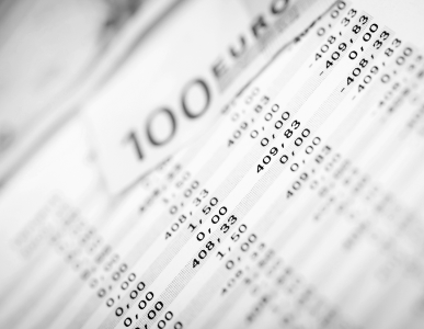 Nahaufnahme eines Kontoauszugs oder Abrechnungsdokuments, auf dem verschiedene Buchungen und Beträge zu sehen sind. Im Hintergrund ist ein 100-Euro-Schein erkennbar. Die Szene symbolisiert regelmäßige Zahlungsverpflichtungen, etwa die monatliche Kreditrate.