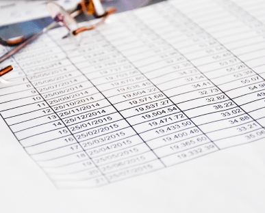 Nahaufnahme eines ausgedruckten Tabellenblatts mit Zahlen, Datumsangaben und Beträgen, das in einem Ordner abgeheftet ist. Die Szene symbolisiert einen Tilgungsplan, der die Rückzahlung eines Kredits über einen bestimmten Zeitraum hinweg detailliert darstellt.