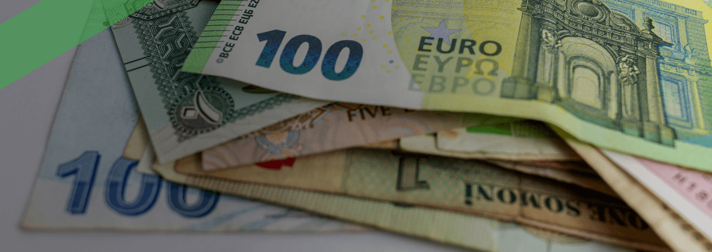 Mehrere Banknoten verschiedener Währungen, darunter ein 100-Euro-Schein, liegen auf einem weißen Untergrund übereinander. Die Szene symbolisiert den internationalen Zahlungsverkehr und Begriffe wie Valuta oder Wertstellung bei Geldtransaktionen.