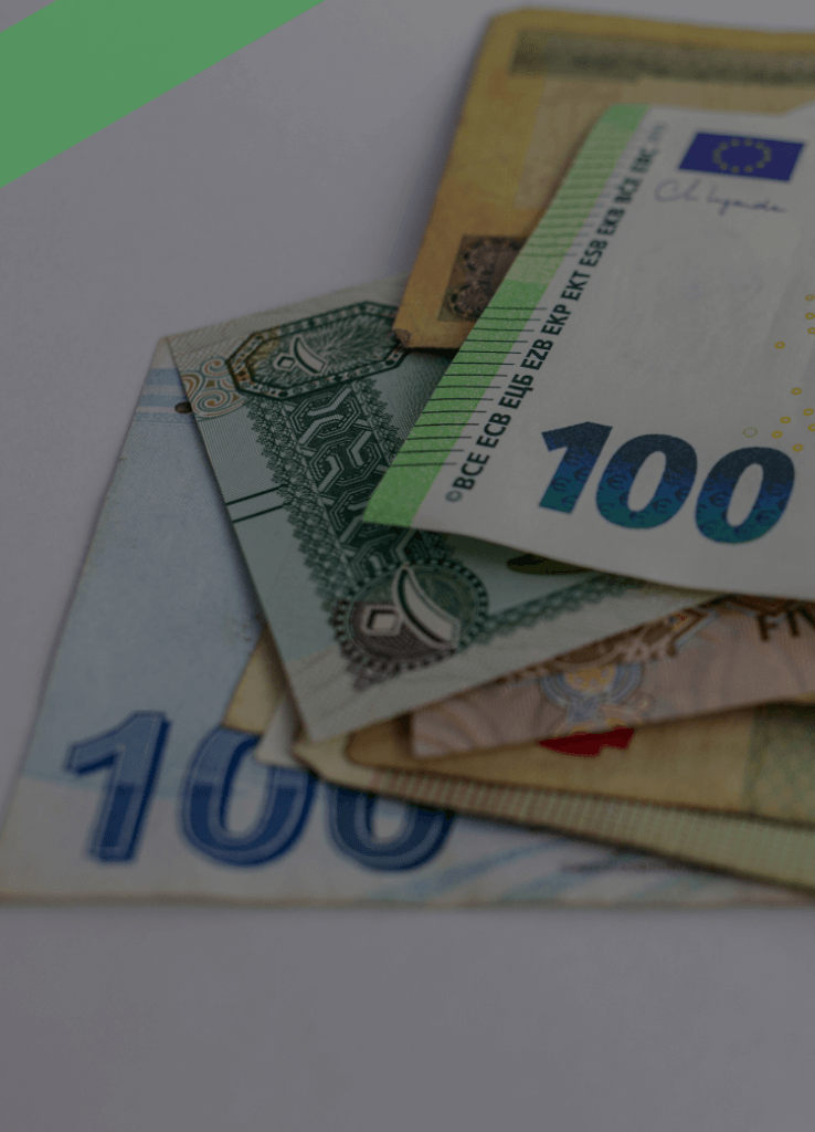 Mehrere Banknoten verschiedener Währungen, darunter ein 100-Euro-Schein, liegen auf einem weißen Untergrund übereinander. Die Szene symbolisiert den internationalen Zahlungsverkehr und Begriffe wie Valuta oder Wertstellung bei Geldtransaktionen.