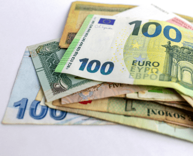 Mehrere Banknoten verschiedener Währungen, darunter ein 100-Euro-Schein, liegen auf einem weißen Untergrund übereinander. Die Szene symbolisiert den internationalen Zahlungsverkehr und Begriffe wie Valuta oder Wertstellung bei Geldtransaktionen.